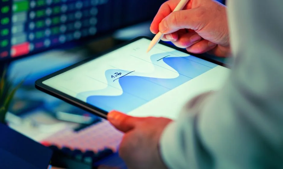 Des mains manipulent une application de trading sur smartphone avec des graphiques, des billets de dollar en arrière-plan.